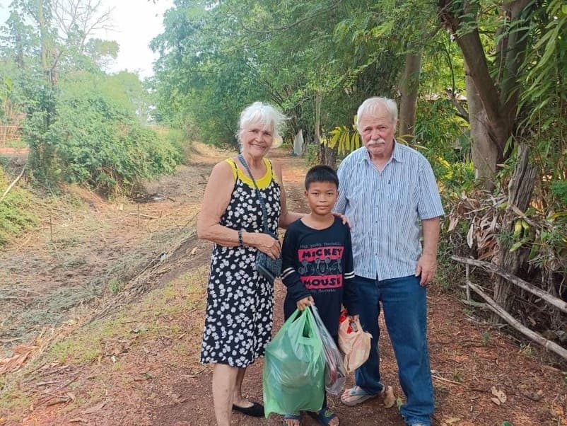 Kathleen and Randy with a boy holding grocery bags on a dirt road