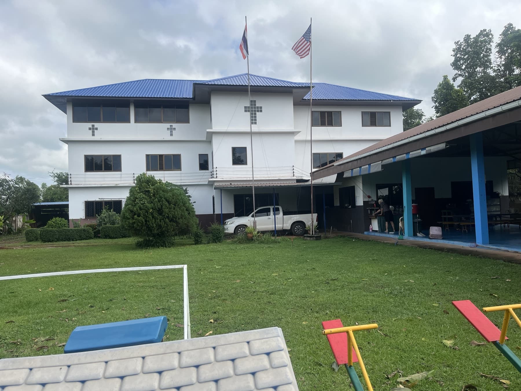 The three-story white home with a blue roof, crosses and flags, lawn and play area